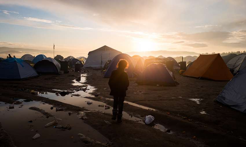 Refugee kid in front of hundreds of tents, during sunrise in a refugee camp in Idomeni, Greece in March 2016. Image by George Tatakis via iStock.